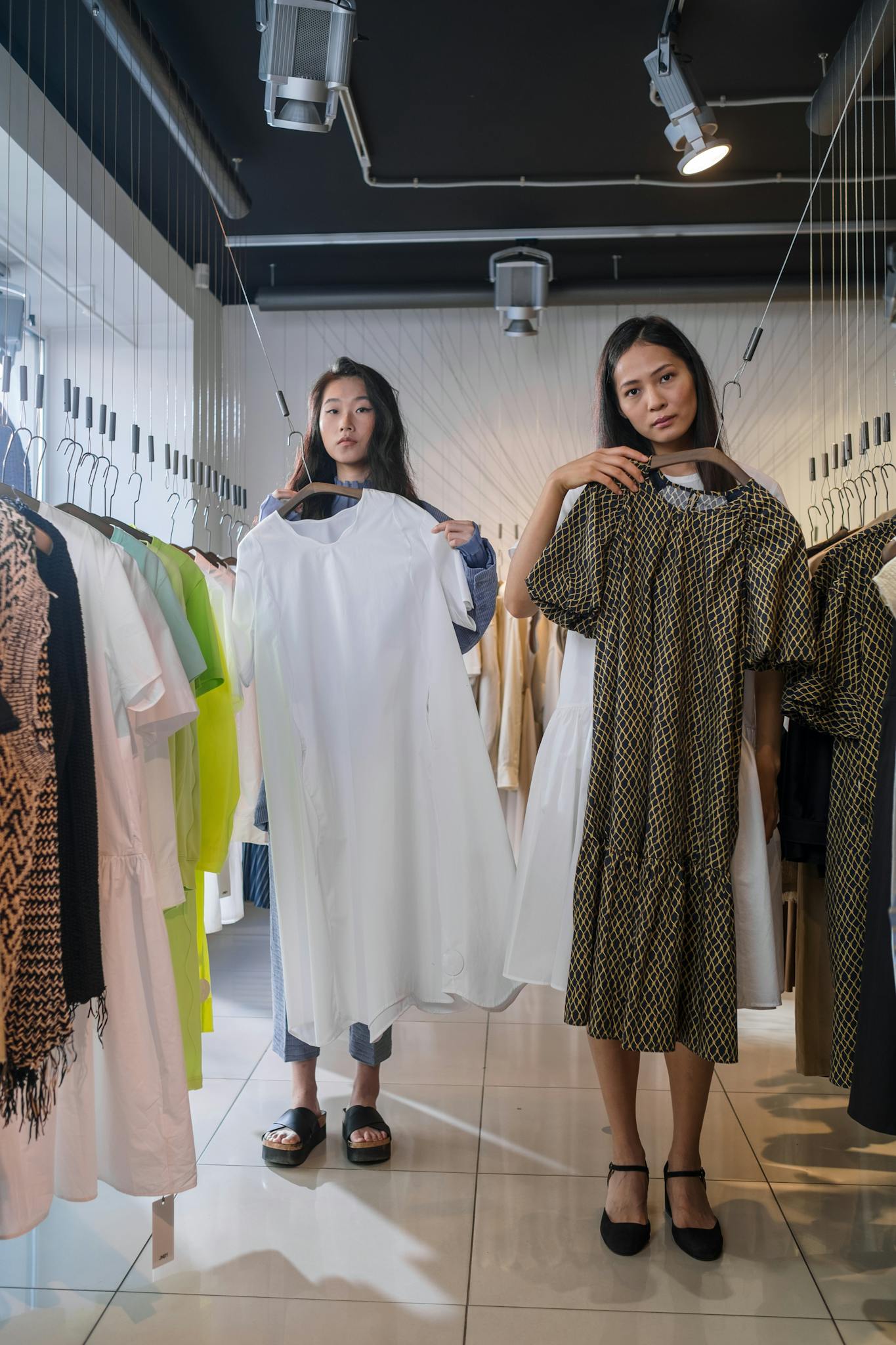 Two women shopping and holding dresses in a stylish boutique's clothing section.